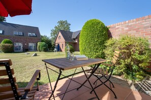 A patio with a table and chairs, a red umbrella, and a brick building in the background. - "Kranich" – Bright Holiday Apartment for Nature Lovers in Usedom's Achterland (Mellenthin)
