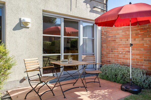 Eine Terrasse mit Tisch und Stühlen, einem roten Sonnenschirm und einer Ziegelwand.