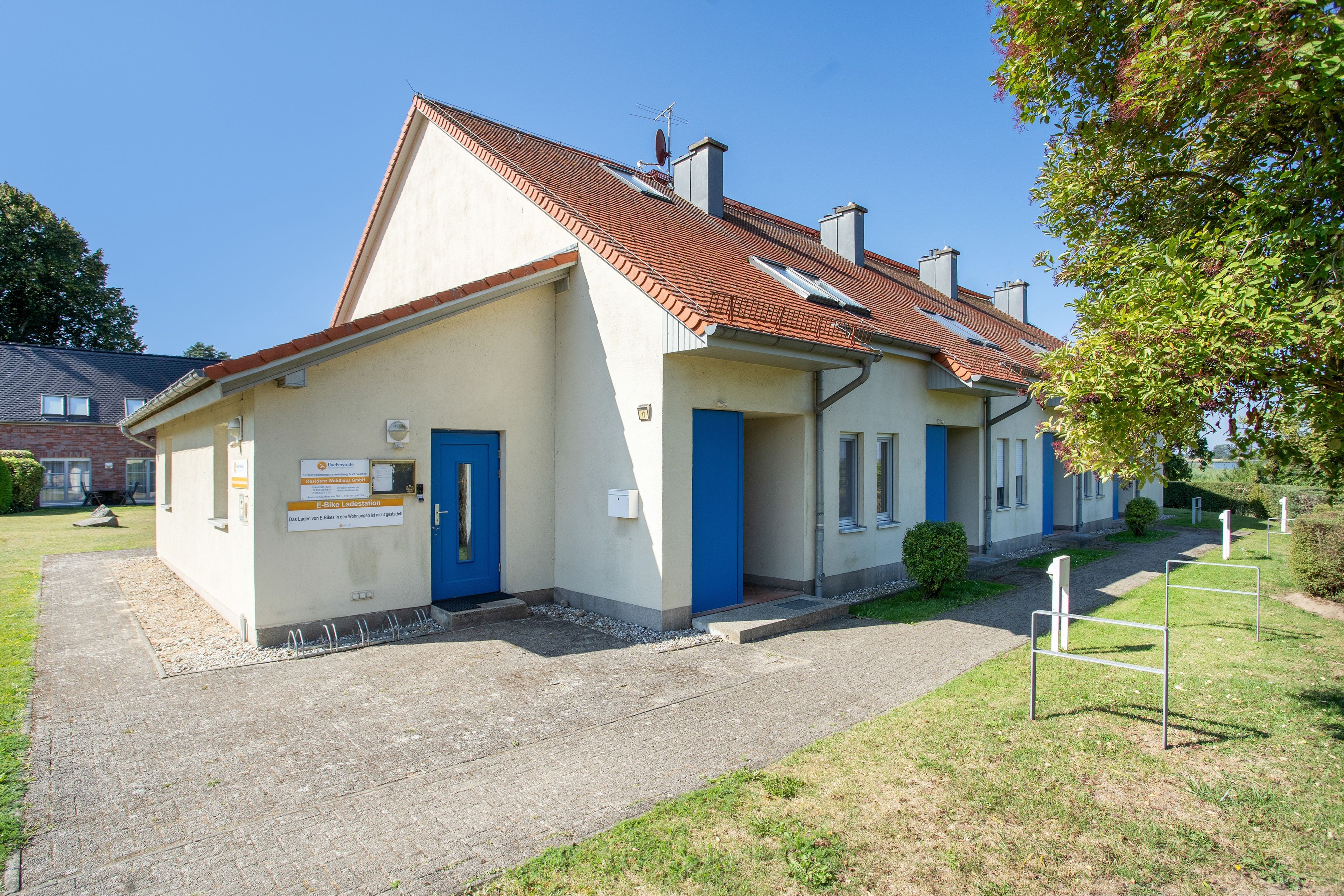 Ein Gebäude mit rotem Ziegeldach, blauer Tür und einem Schild, das eine E-Bike-Ladestation kennzeichnet.
