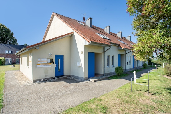 A building with a red-tiled roof, a blue door, and a sign indicating an E-Bike Ladestation. - "Kranich" – Bright Holiday Apartment for Nature Lovers in Usedom's Achterland (Mellenthin)
