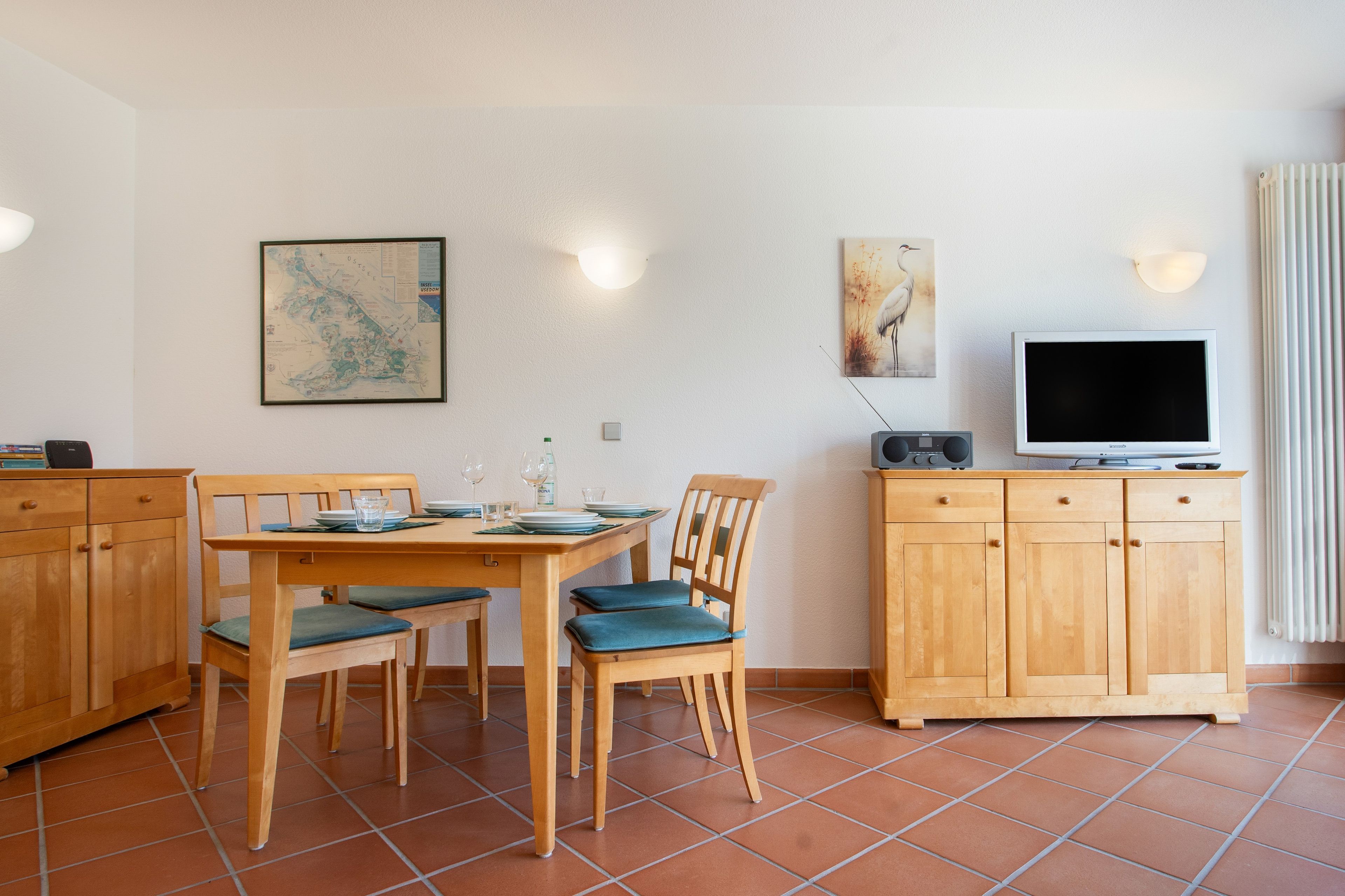 Ein Essbereich mit einem Holztisch und Stühlen, einem Fernseher auf einem Schrank und einer Karte an der Wand.