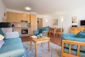 A modern living room with a sofa, a coffee table, and a dining area with a table and chairs. - "Kranich" – Bright Holiday Apartment for Nature Lovers in Usedom's Achterland (Mellenthin)