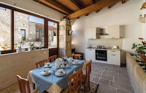 A dining area with a table set for four, a kitchen with white cabinets, and a stone wall. - Vacation Home in Comiso with 3 bedrooms sleeps 7 (Comiso)