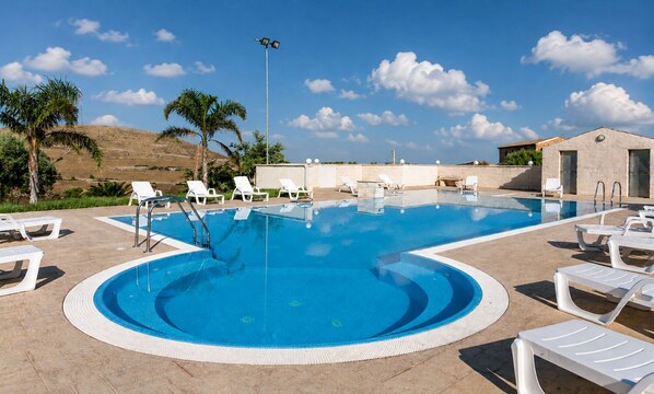 Una piscina con lettini e un palo, circondata da un muro di pietra e palme.
