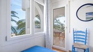 Une chambre comprenant un lit, une chaise, une fenêtre donnant sur des palmiers et une porte menant à un espace extérieur.