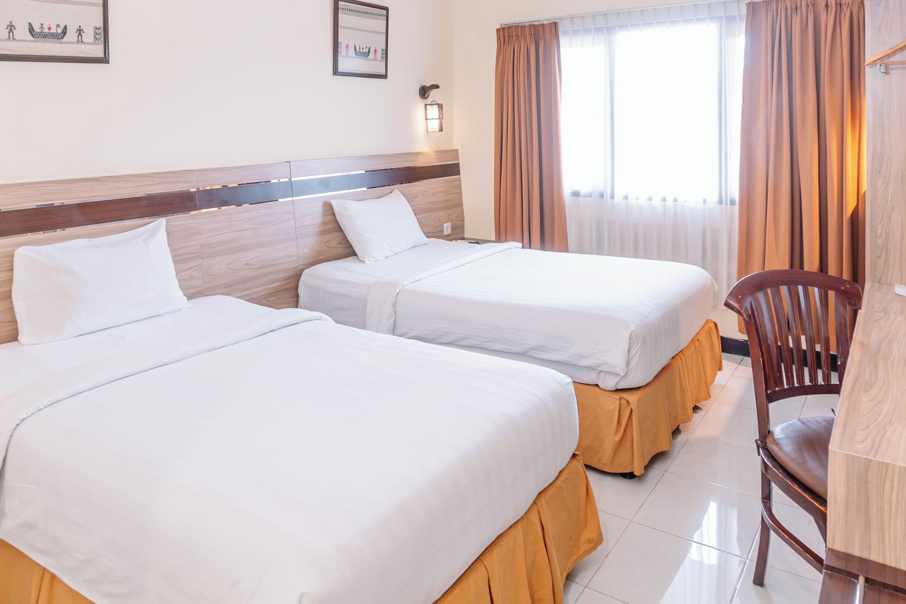 A hotel room with two beds, a wooden headboard, a desk, and a chair.