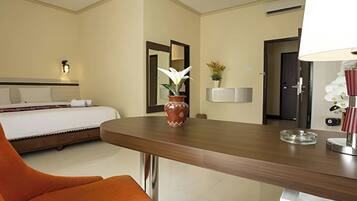 Habitación de hotel con una cama, un escritorio de madera, un florero con una flor, un espejo y una lámpara.