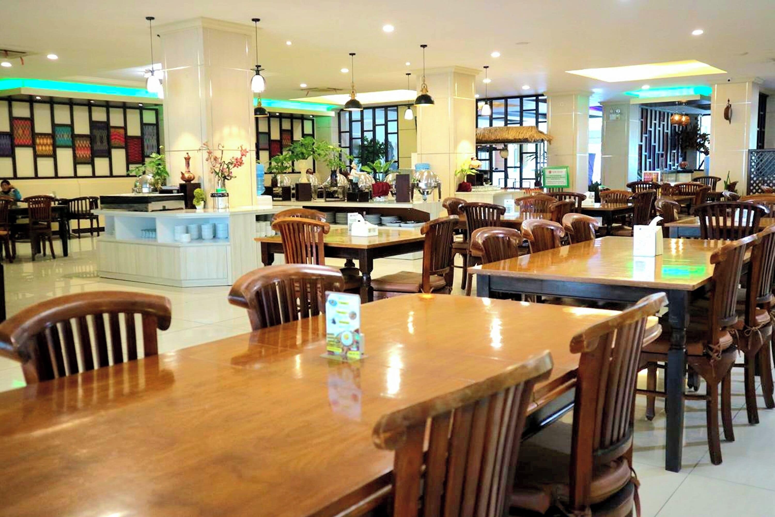 A spacious restaurant with wooden tables and chairs, a central counter, and decorative plants.