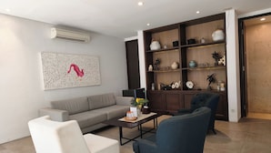 Una sala de estar con un sofá, dos sillones, una mesa de centro y una estantería de madera con objetos decorativos.
