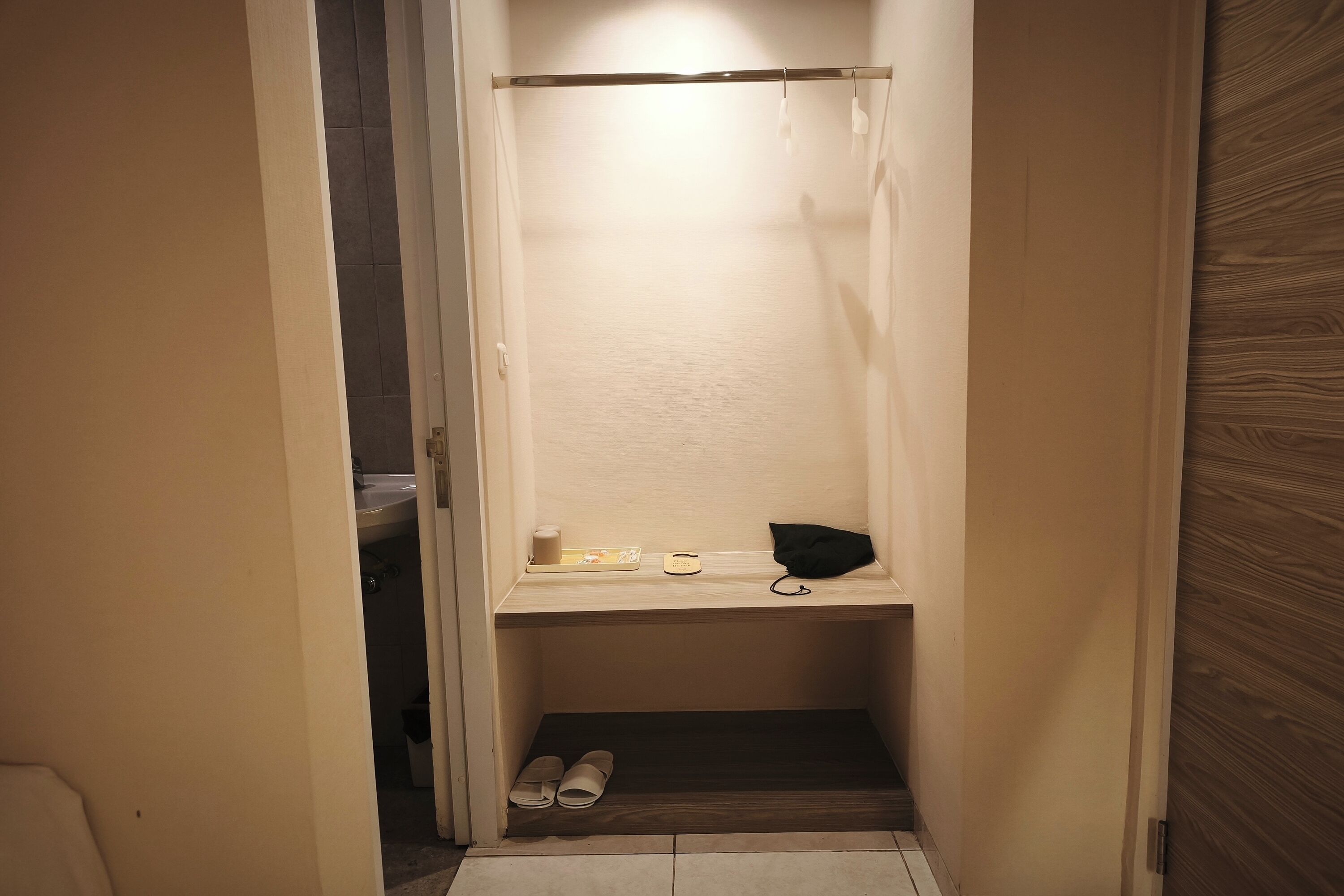 Een smalle inloopkast met een plank, een paar schoenen en een zwarte tas.