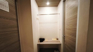 Un pasillo estrecho con una puerta de madera, un estante pequeño con una bolsa negra, un par de zapatillas y un perchero.