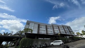 Un edificio con un letrero que dice 'PUBLIC GOURMET' y un coche blanco estacionado adelante.