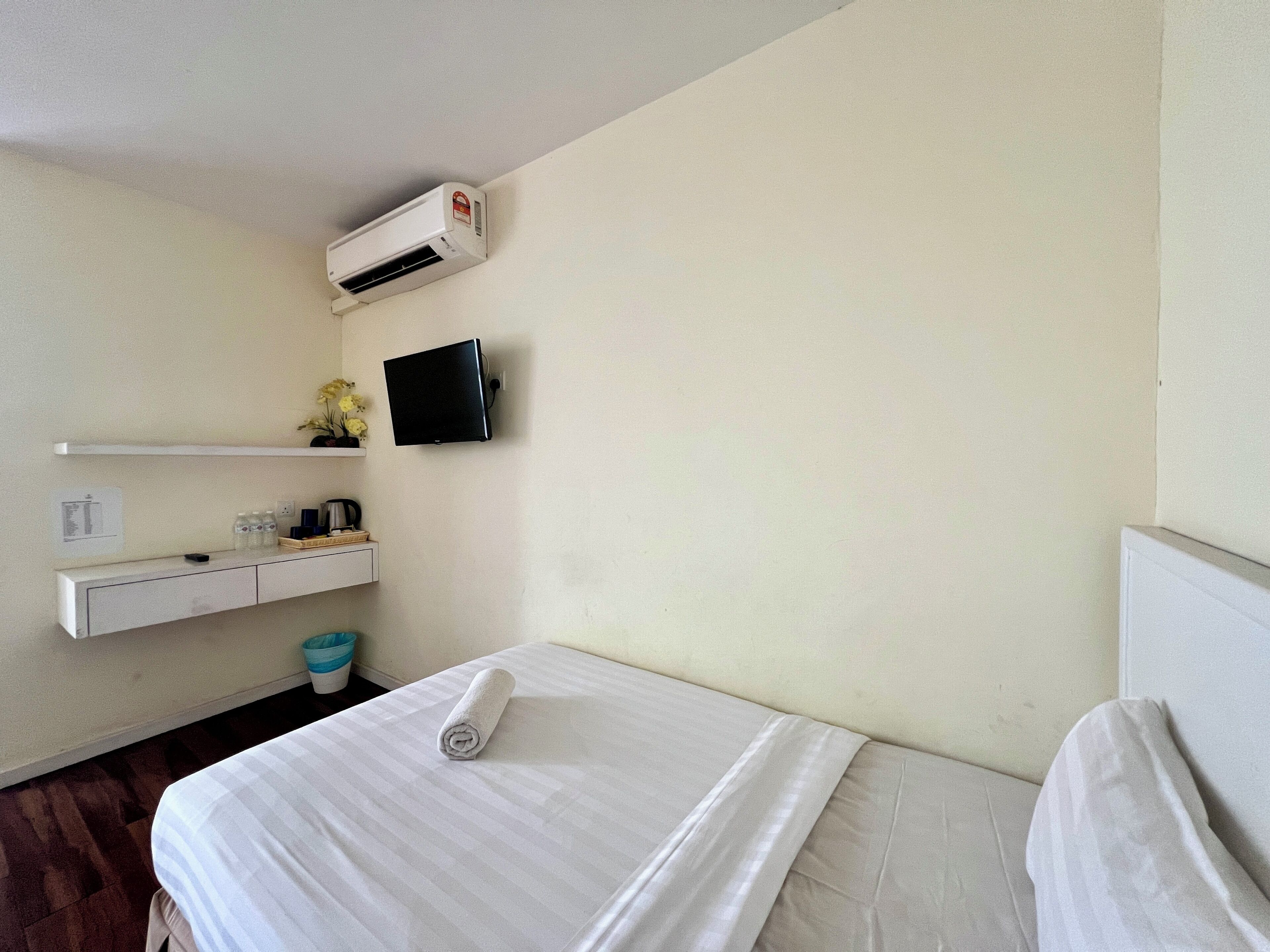 Une chambre d’hôtel équipée d’un lit, d’un téléviseur fixé au mur, d’une petite étagère avec des articles de toilette et d’un appareil de climatisation.