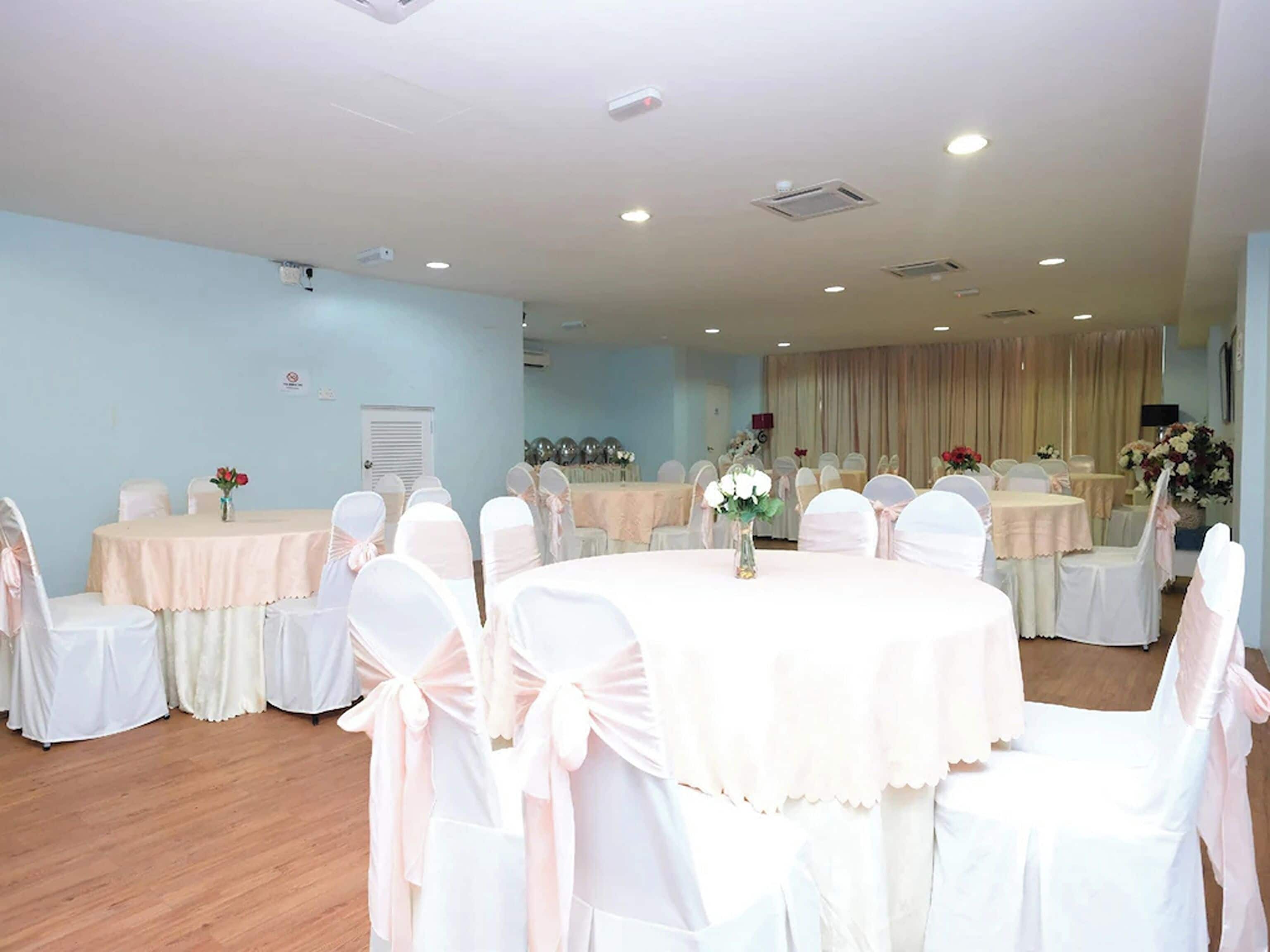 A banquet hall with round tables, white chairs with pink sashes, and floral centerpieces.