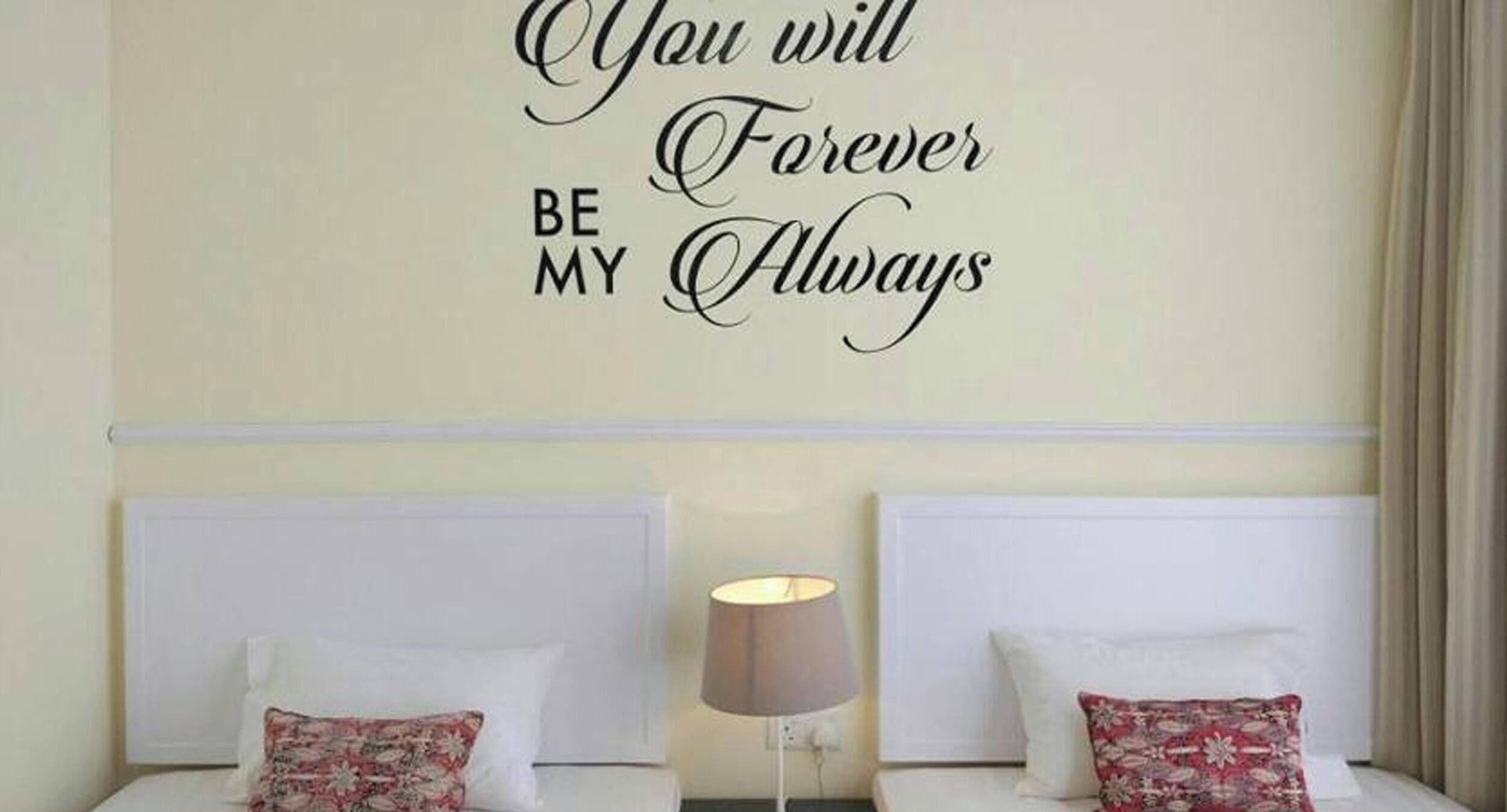 A hotel room with a bed, a bedside lamp, and a wall with a motivational quote.