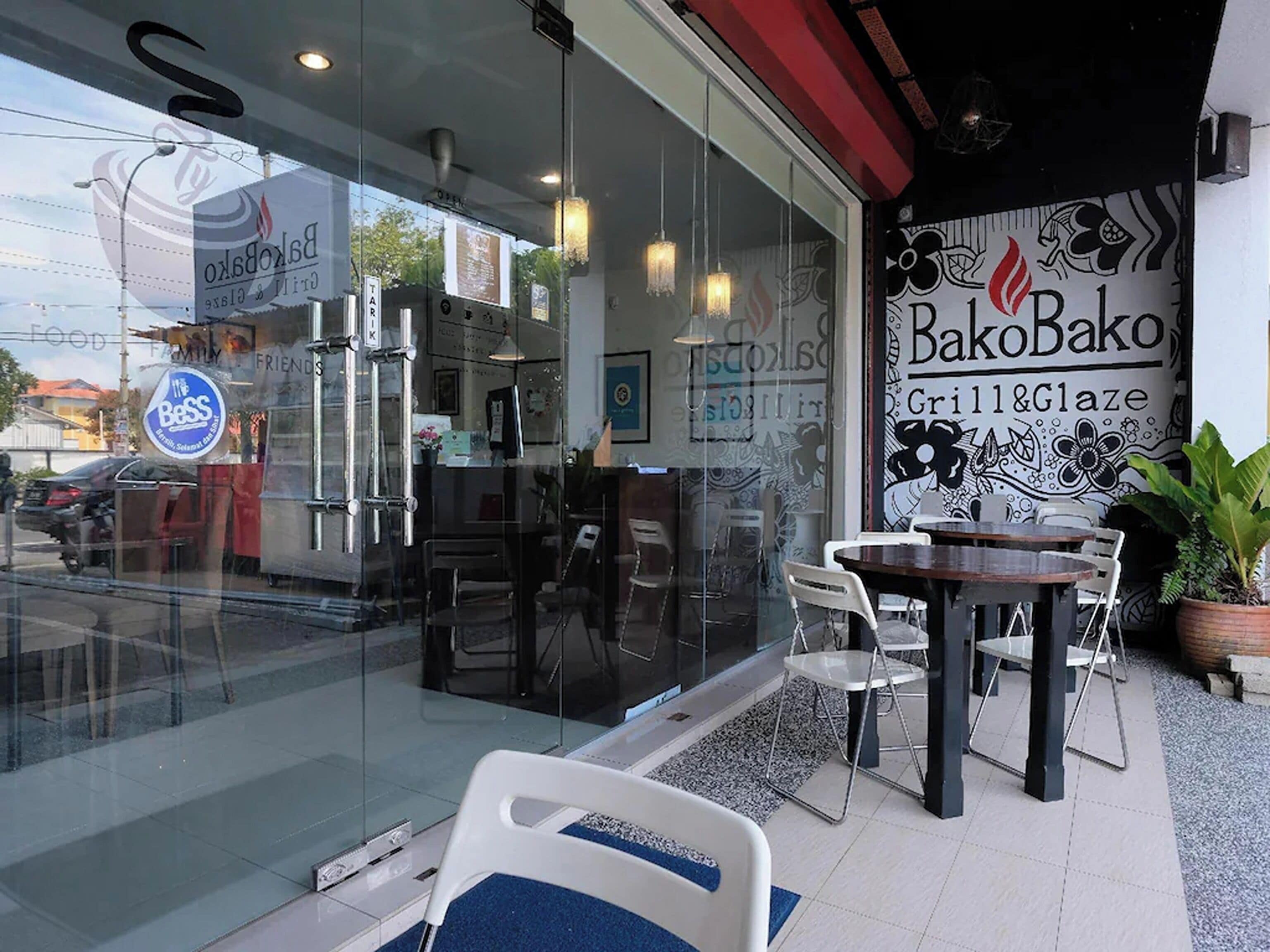 A restaurant with a glass facade, outdoor seating, and a mural on the wall.