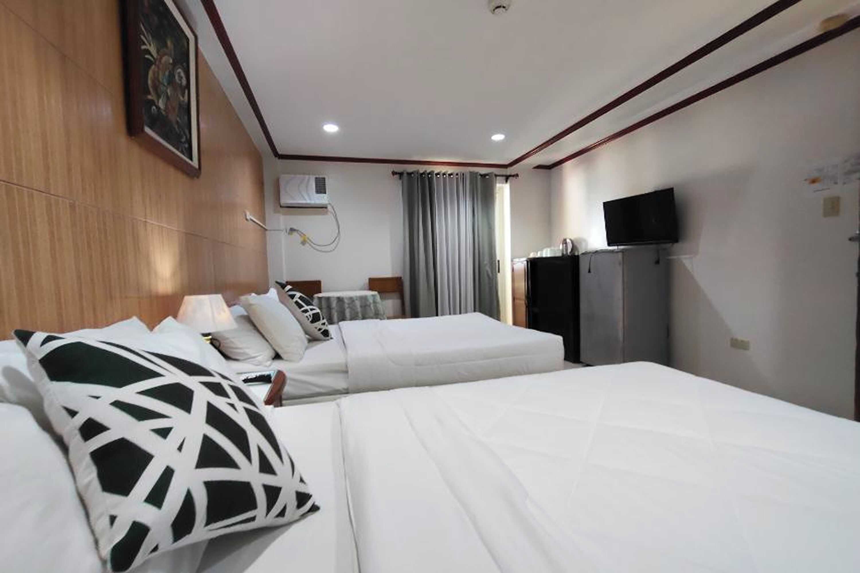 A hotel room with two beds, a television, a desk, and a window with curtains.