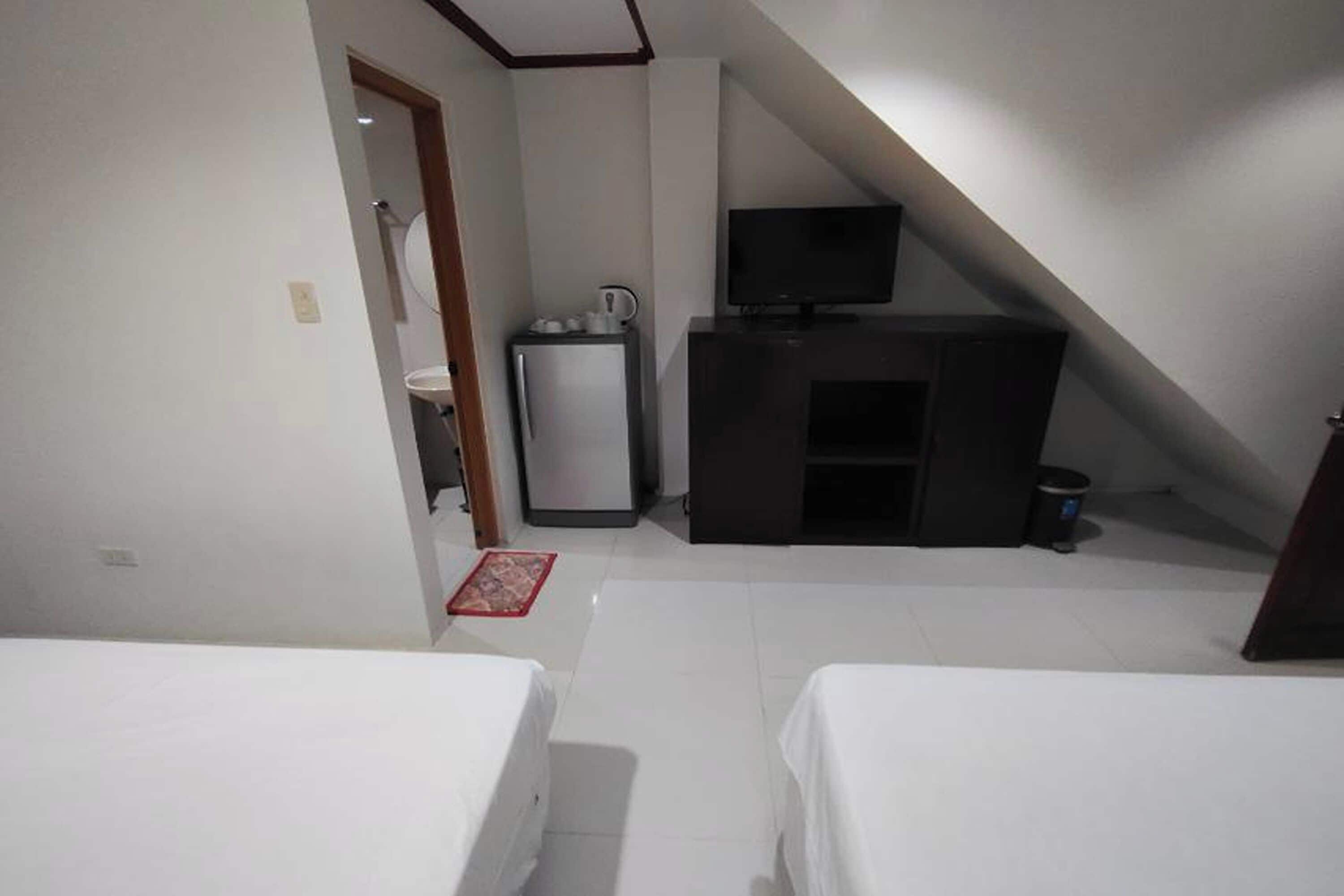 Una habitación con dos camas, una kitchenette pequeña con refrigerador, un televisor y una puerta que da a otra habitación.