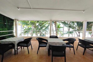 A restaurant with outdoor seating, white tables, and black chairs, overlooking palm trees. - Shenna's Beach Resort Boracay (Boracay Island)