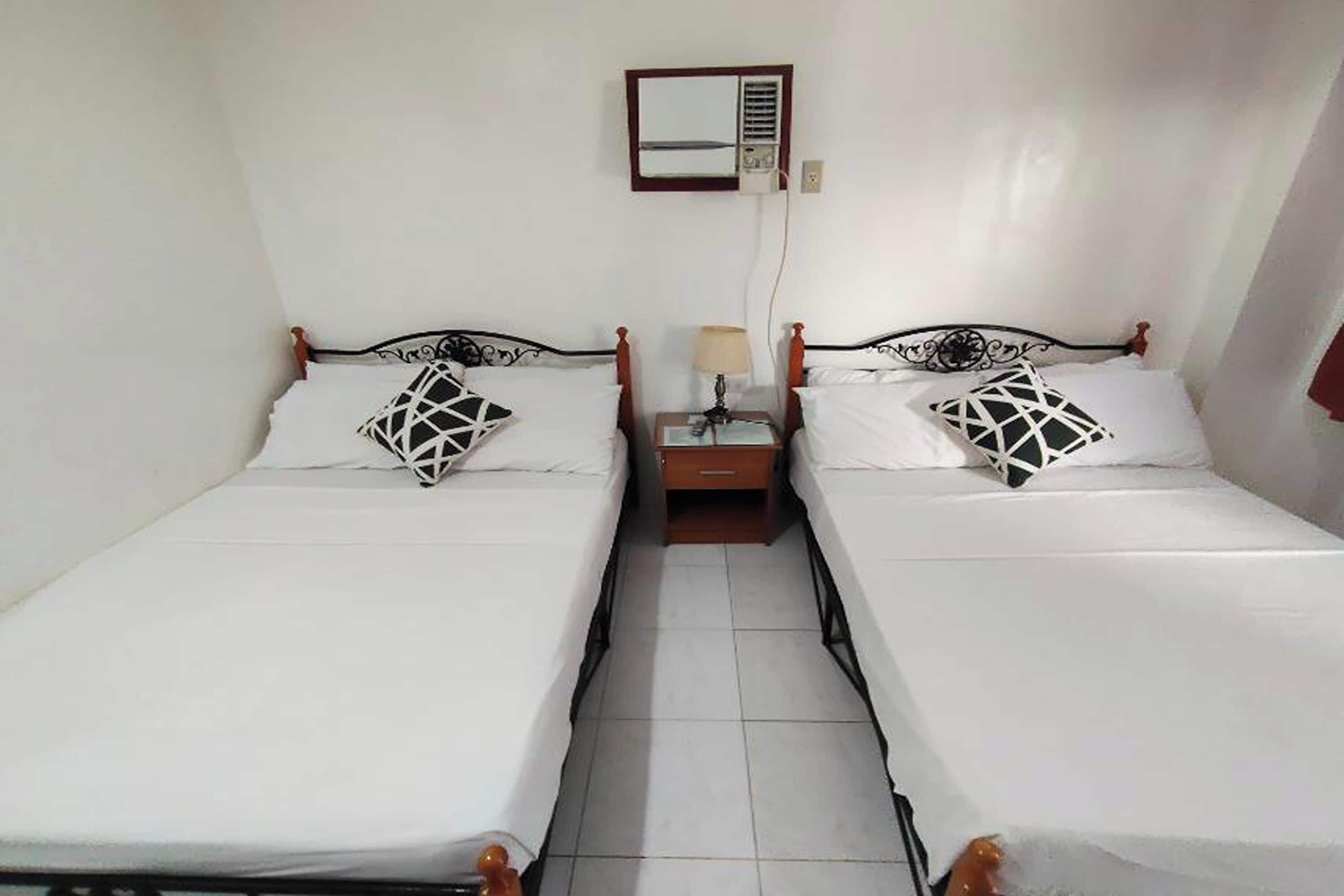 Una habitación con dos camas individuales, una mesita de noche con lámpara, un espejo y un calentador en la pared.