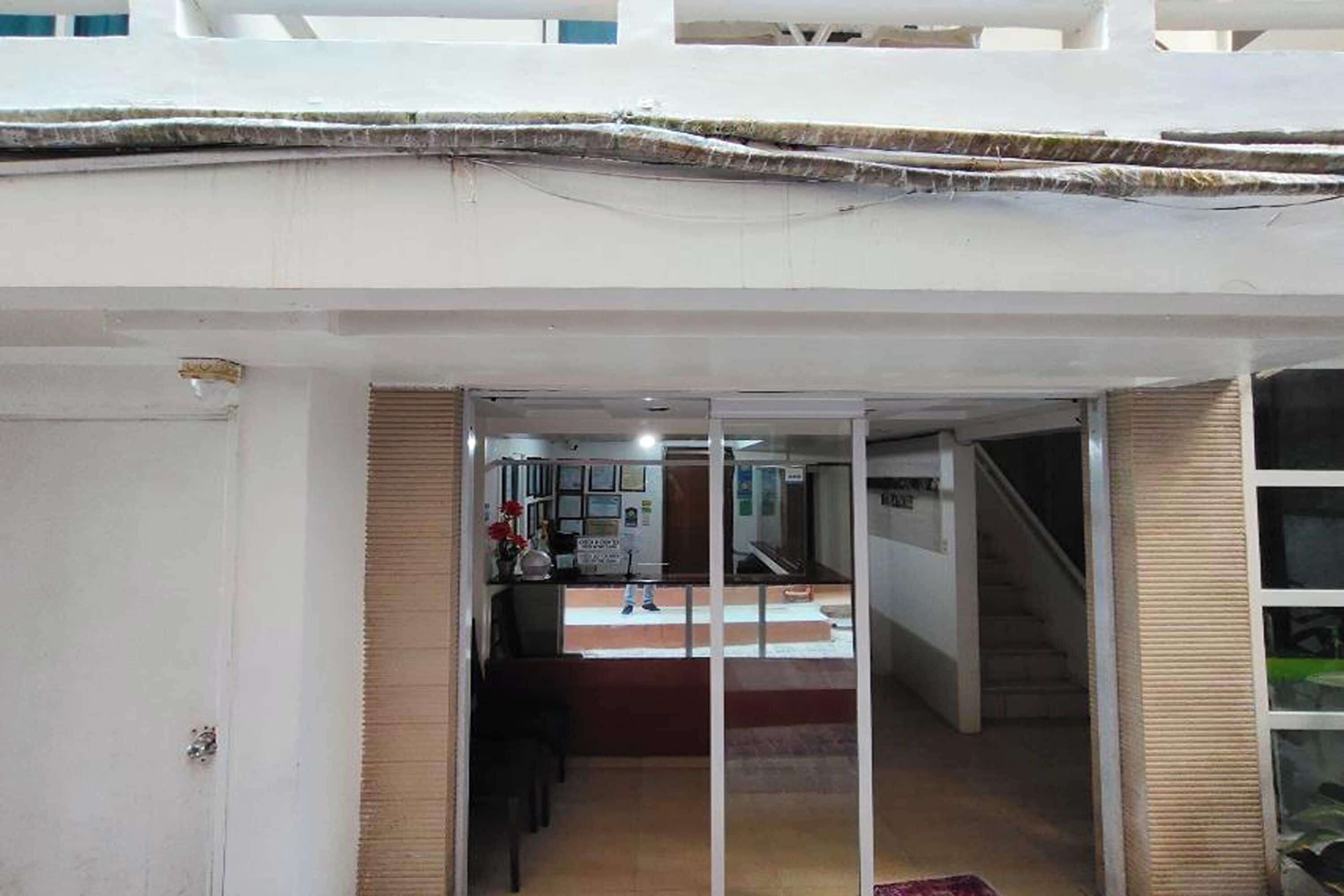 A hotel interior with a reception desk, a staircase, and a view of the interior through a glass door.