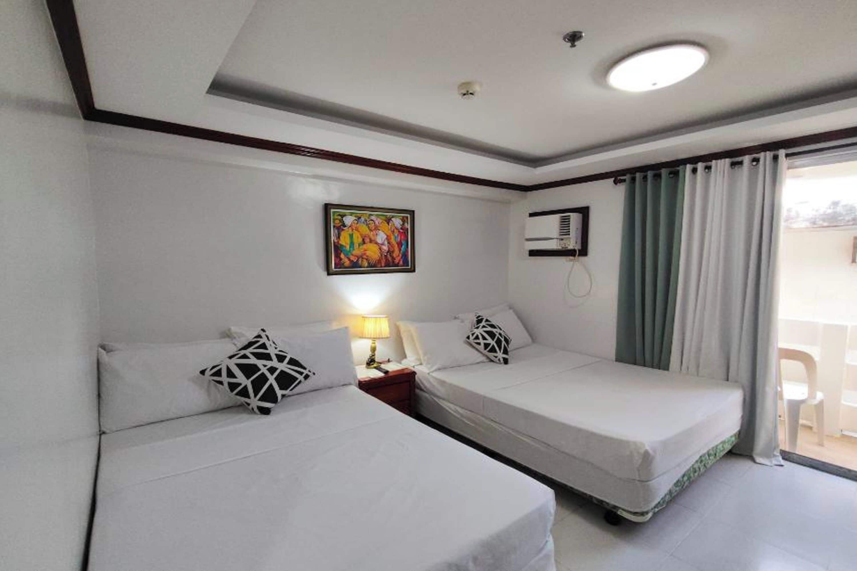 Una habitación con dos camas, un cuadro en la pared, un equipo de aire acondicionado y una ventana con cortinas.