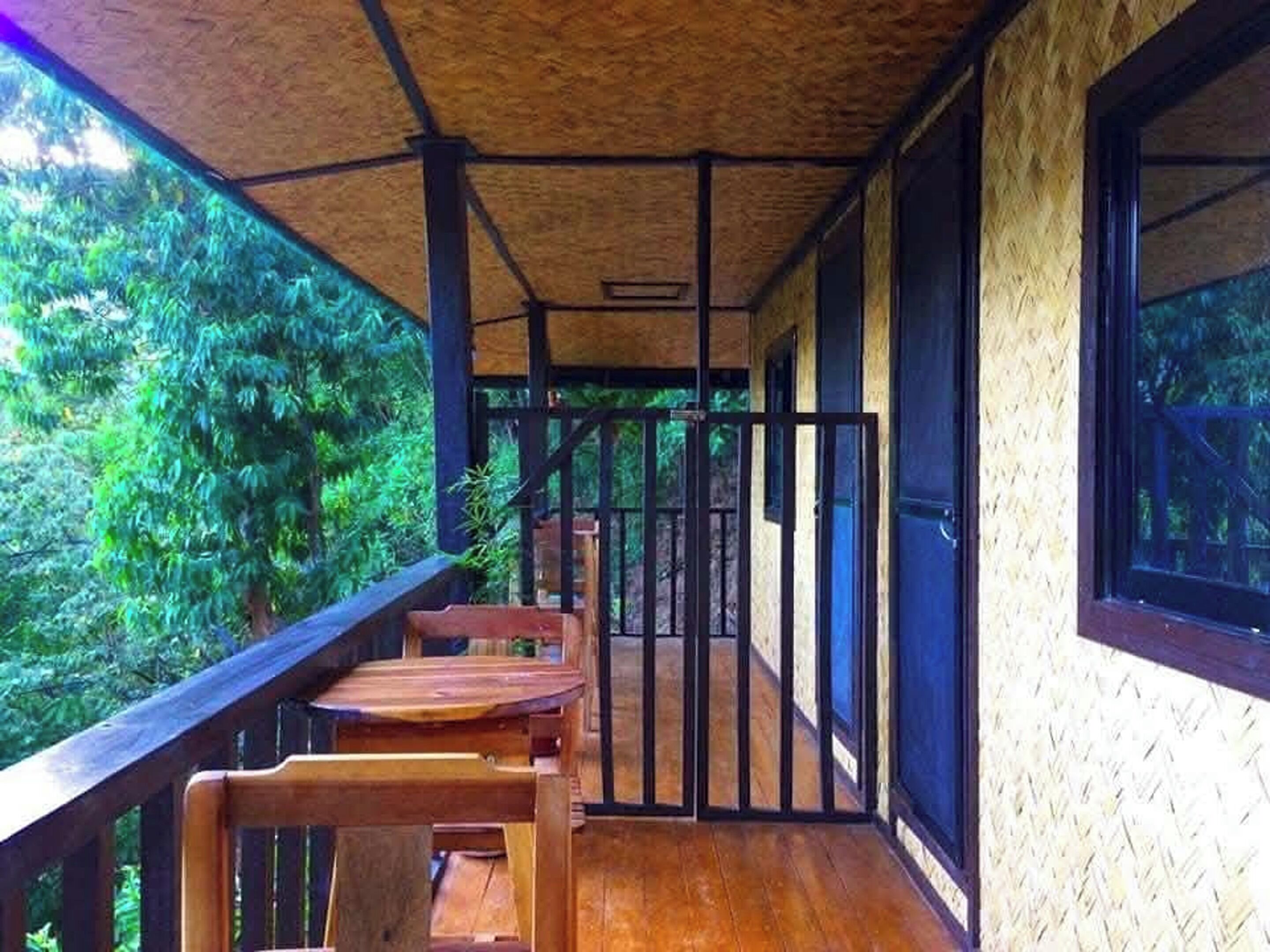 Um deck de madeira com mesa e cadeiras, uma porta de vidro e vista para o verde.