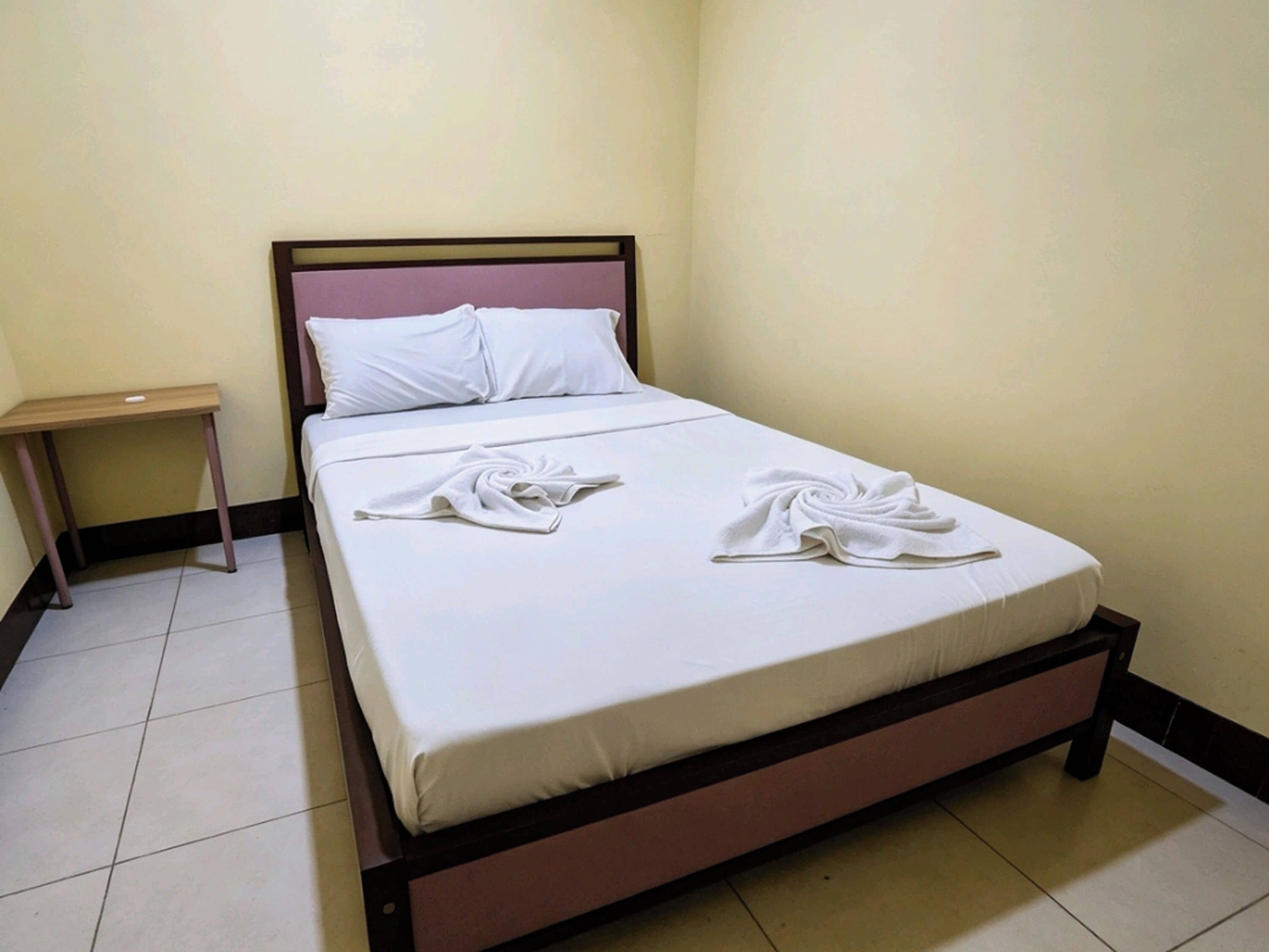 A single bed with a wooden frame, white bedding, and two towels folded on the bed.
