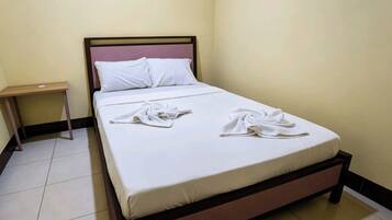 A single bed with a wooden frame, white bedding, and two towels folded on the bed.