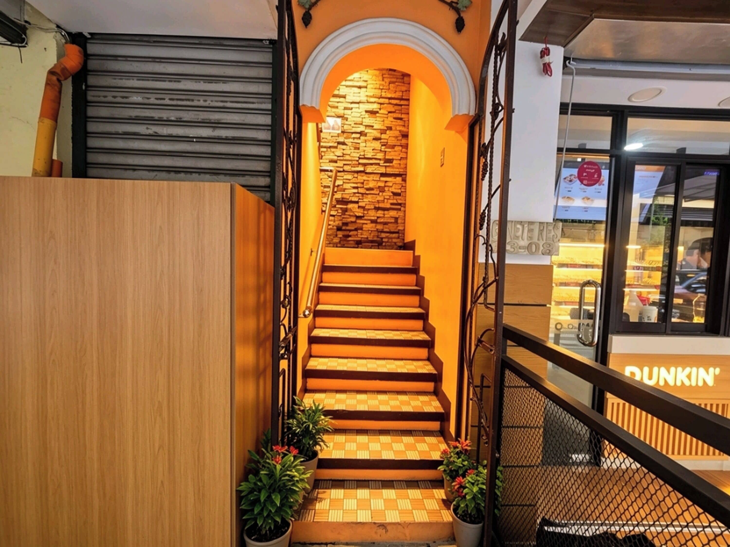 Eine Treppe mit Schachbrettmuster, die zu einer Steinmauer führt, gesäumt von Blumentöpfen und einem Metallgeländer.