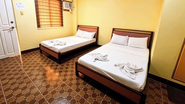 A hotel room with two single beds, a window with blinds, an air conditioning unit, and a tiled floor. - Nook Airport Guesthouse (Pasay)