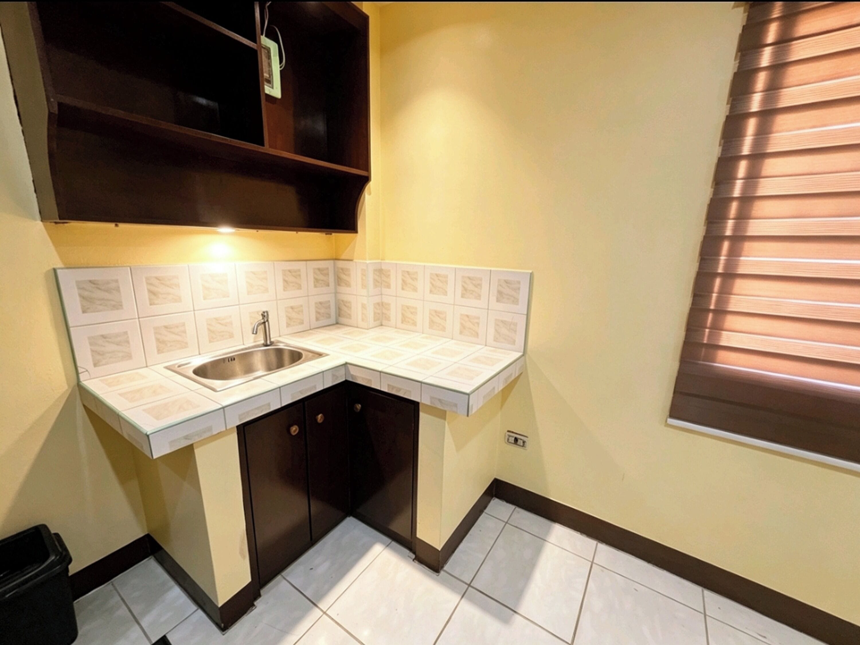 A compact kitchen with a sink, cabinets, and a window with blinds.
