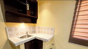 A compact kitchen with a sink, cabinets, and a window with blinds. - Nook Airport Guesthouse (Pasay)