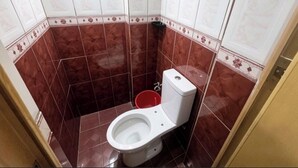 A small bathroom with a toilet, a red bucket, and a corner sink. - Nook Airport Guesthouse (Pasay)