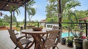 A covered outdoor seating area with a pool view, wooden furniture, and potted plants. - Para Hill Homestay (Pa Klok)