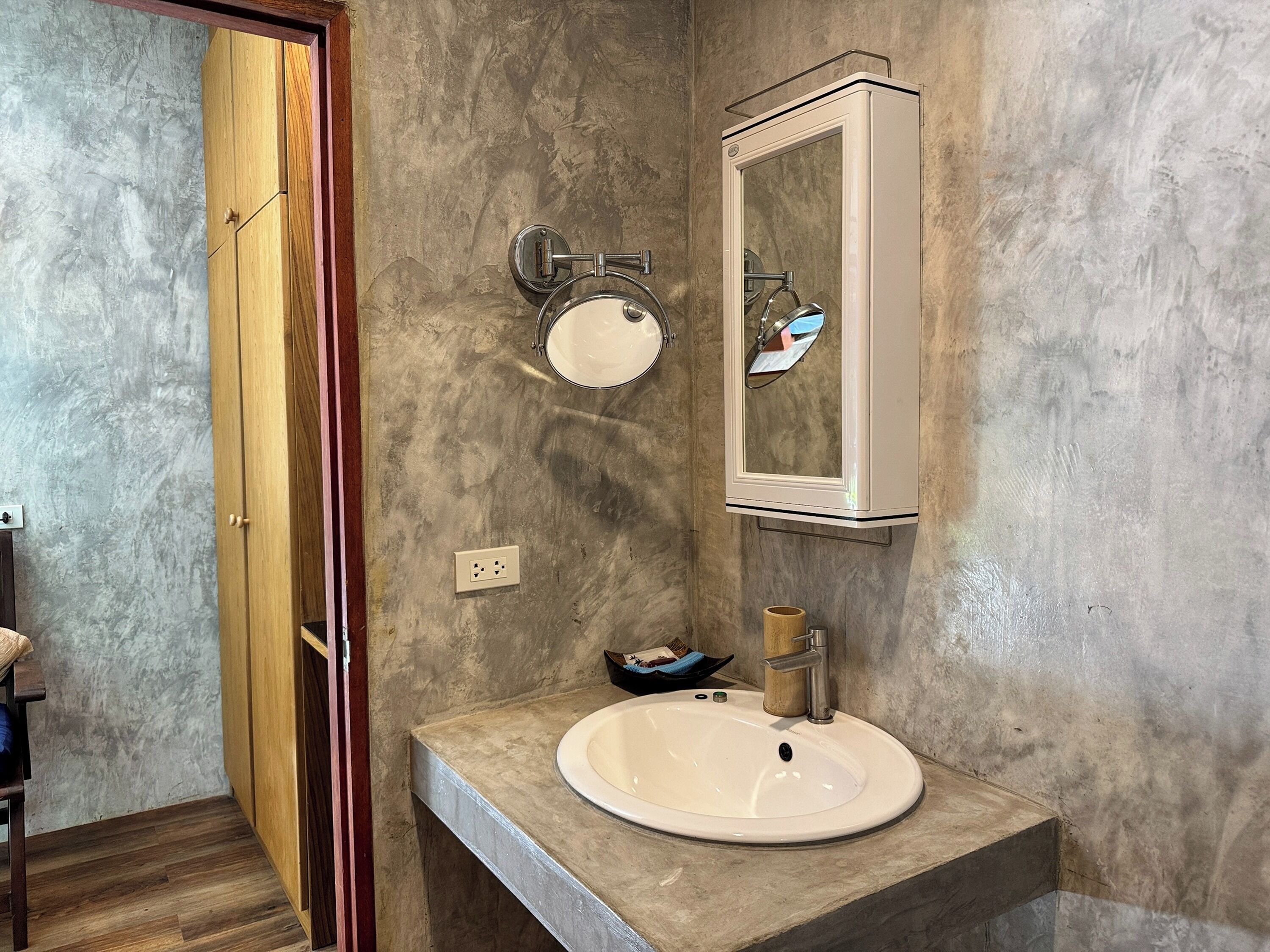 A bathroom with a wooden door, a round mirror, a white sink, and a cabinet.