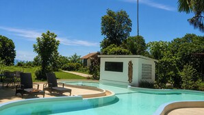 A swimming pool with lounge chairs, a small building with a statue, and surrounding greenery. - Para Hill Homestay (Pa Klok)