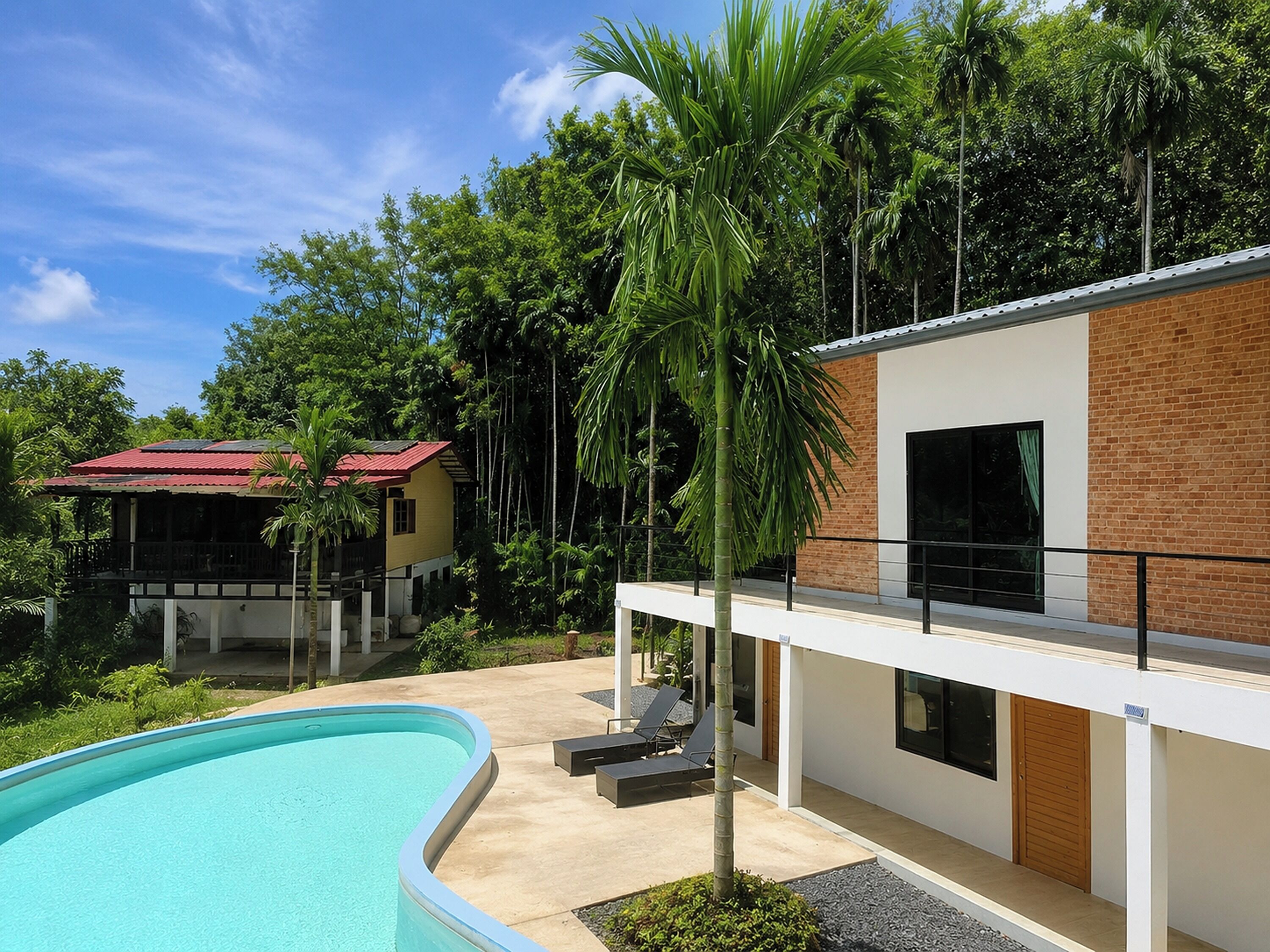 Un edificio moderno con piscina, una estructura de techo rojo y abundante vegetación.