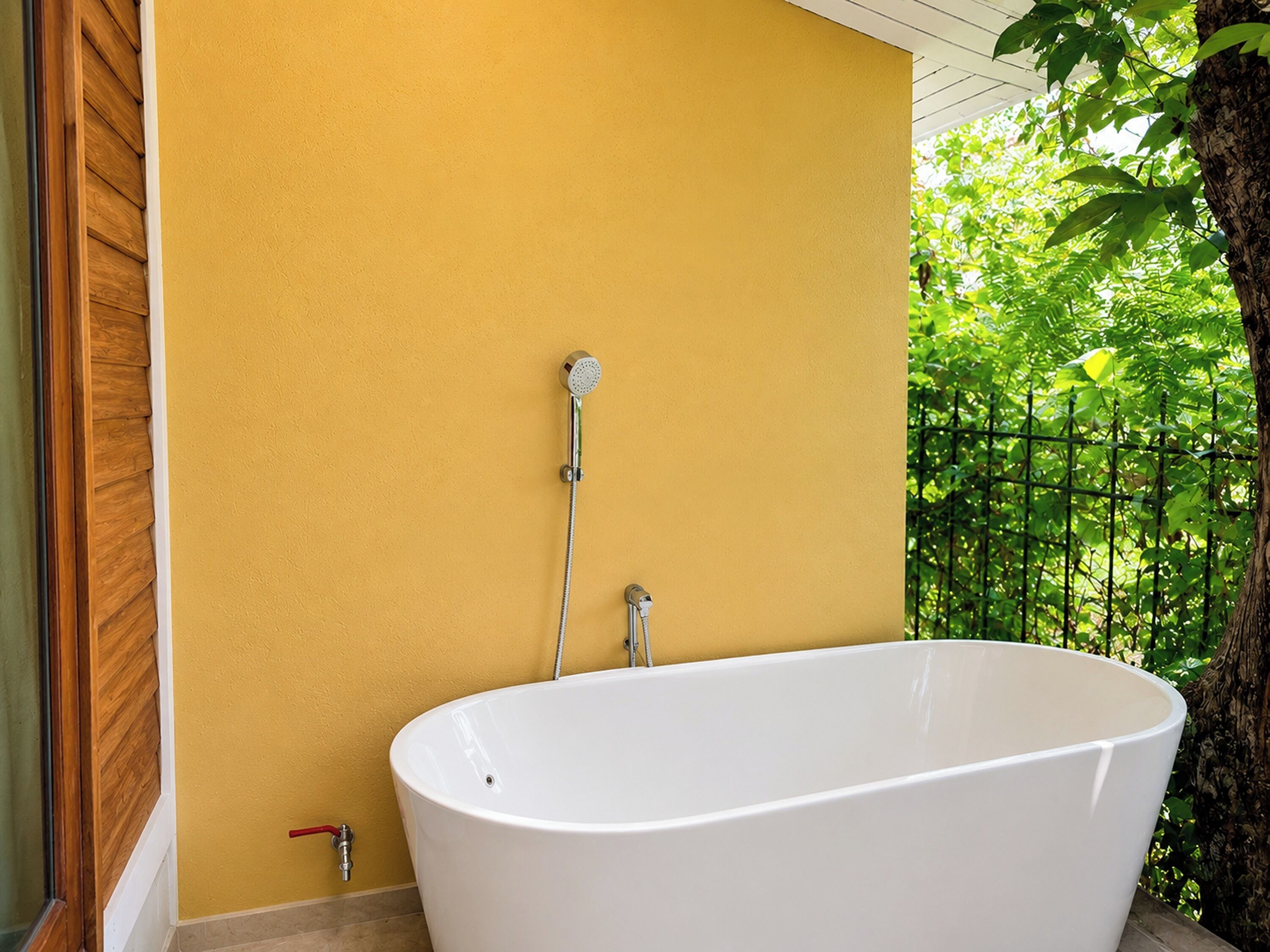 A white freestanding bathtub in a room with yellow walls and a view of greenery.