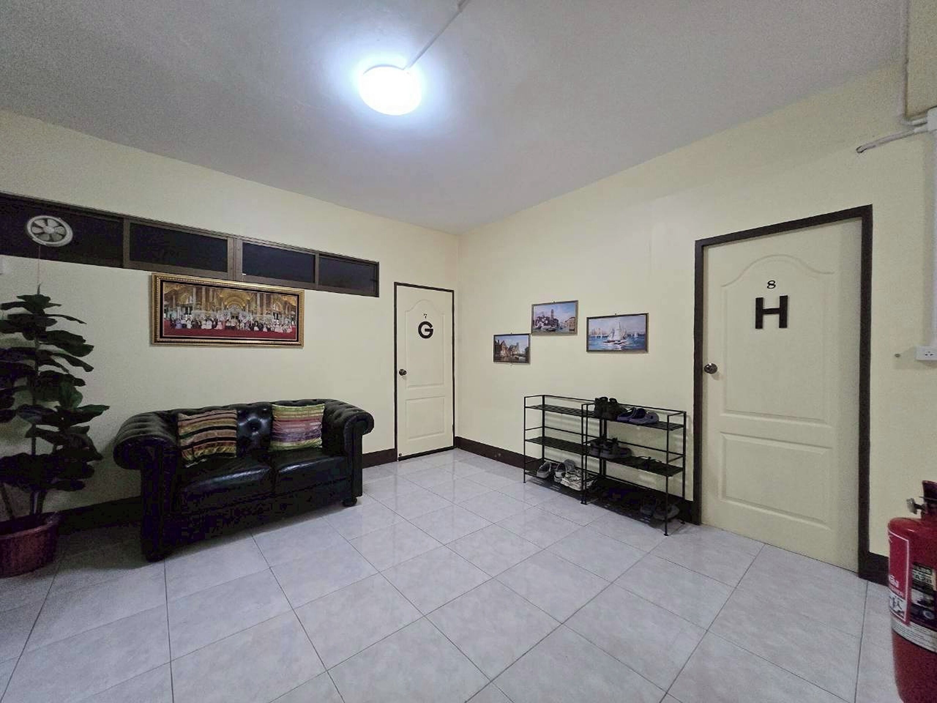 A hotel lobby with a tiled floor, a black leather sofa, a shoe rack, and a door marked with a 'G' and 'H'.