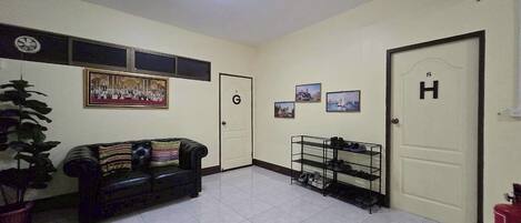 A hotel lobby with a tiled floor, a black leather sofa, a shoe rack, and a door marked with a 'G' and 'H'.