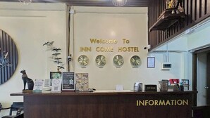 Una recepción con un cartel que dice 'Welcome To INN COME HOSTEL', relojes que marcan diferentes países y un buzón de propinas en la barra.