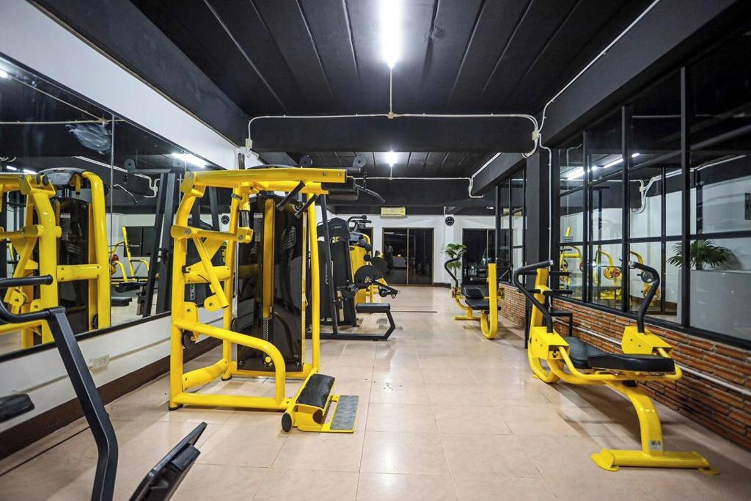 A gym with yellow equipment, mirrors, and a tiled floor.