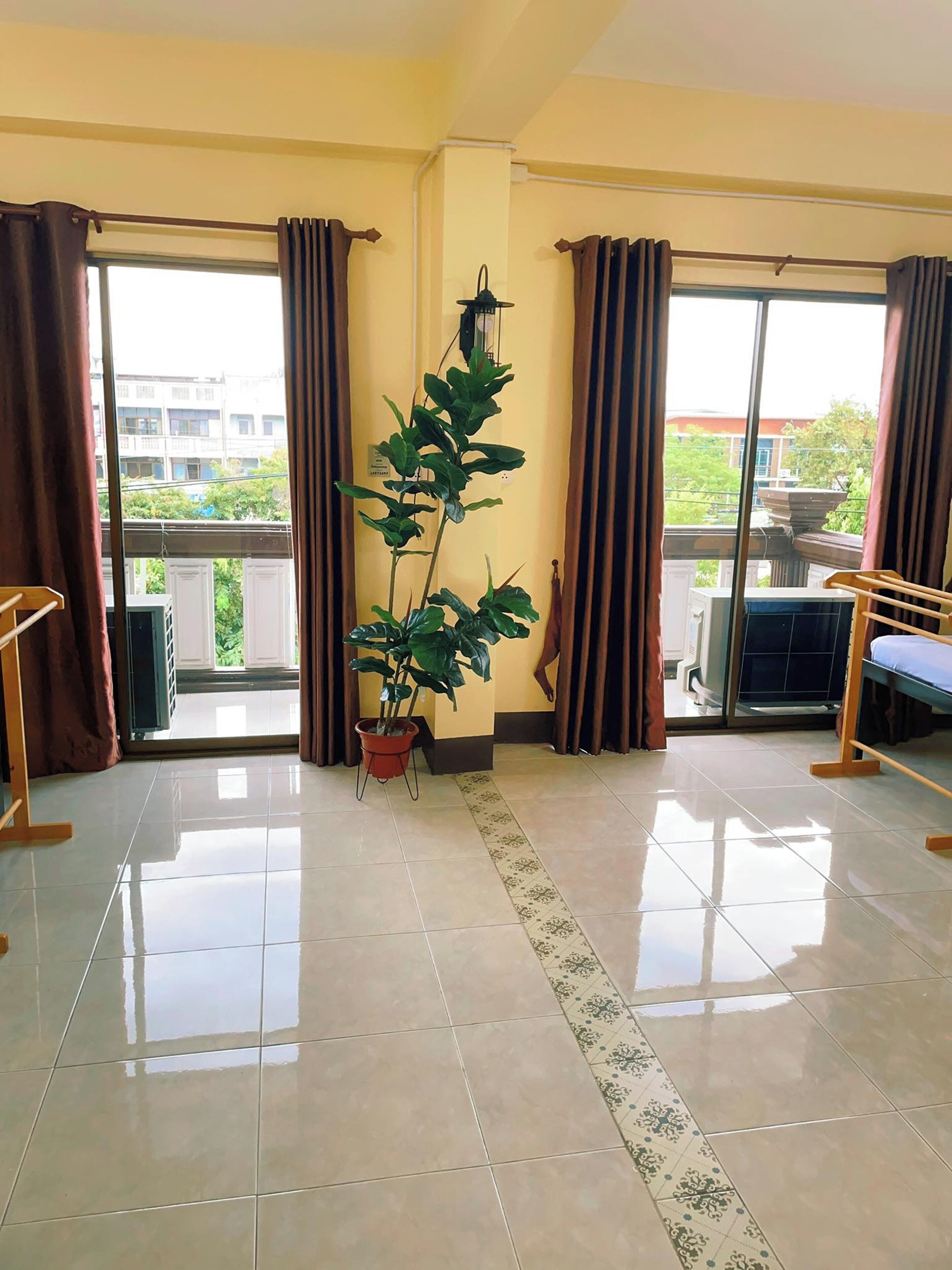 Quarto com planta em vaso, cama, janela com cortinas e piso de azulejos.