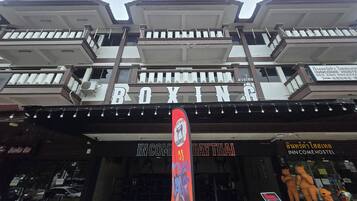 Um edifício com uma placa indicando 'BOXING INCOME HOSTEL' e 'DAY THAI', revelando um hostel com temática de boxe e um restaurante tailandês.
