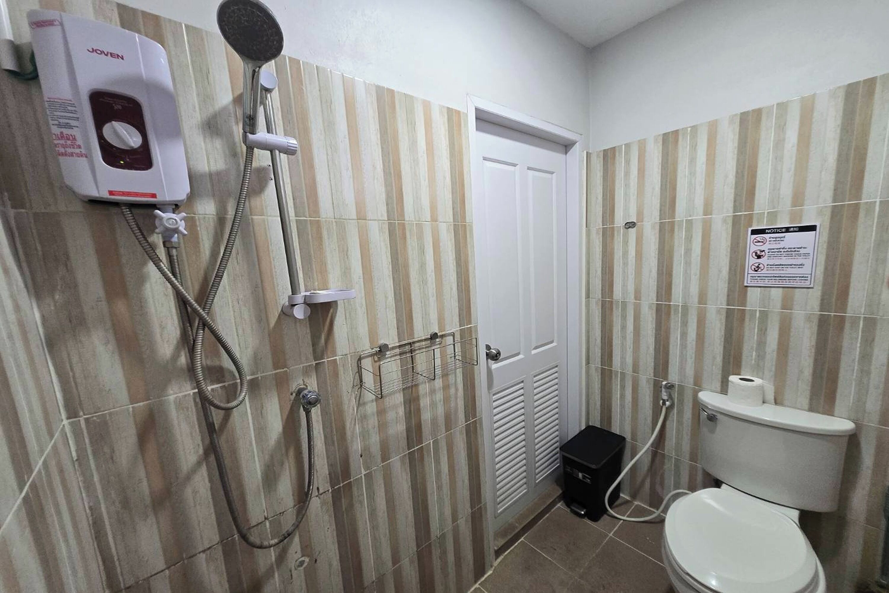 A bathroom with a shower, toilet, and a notice sign on the wall.