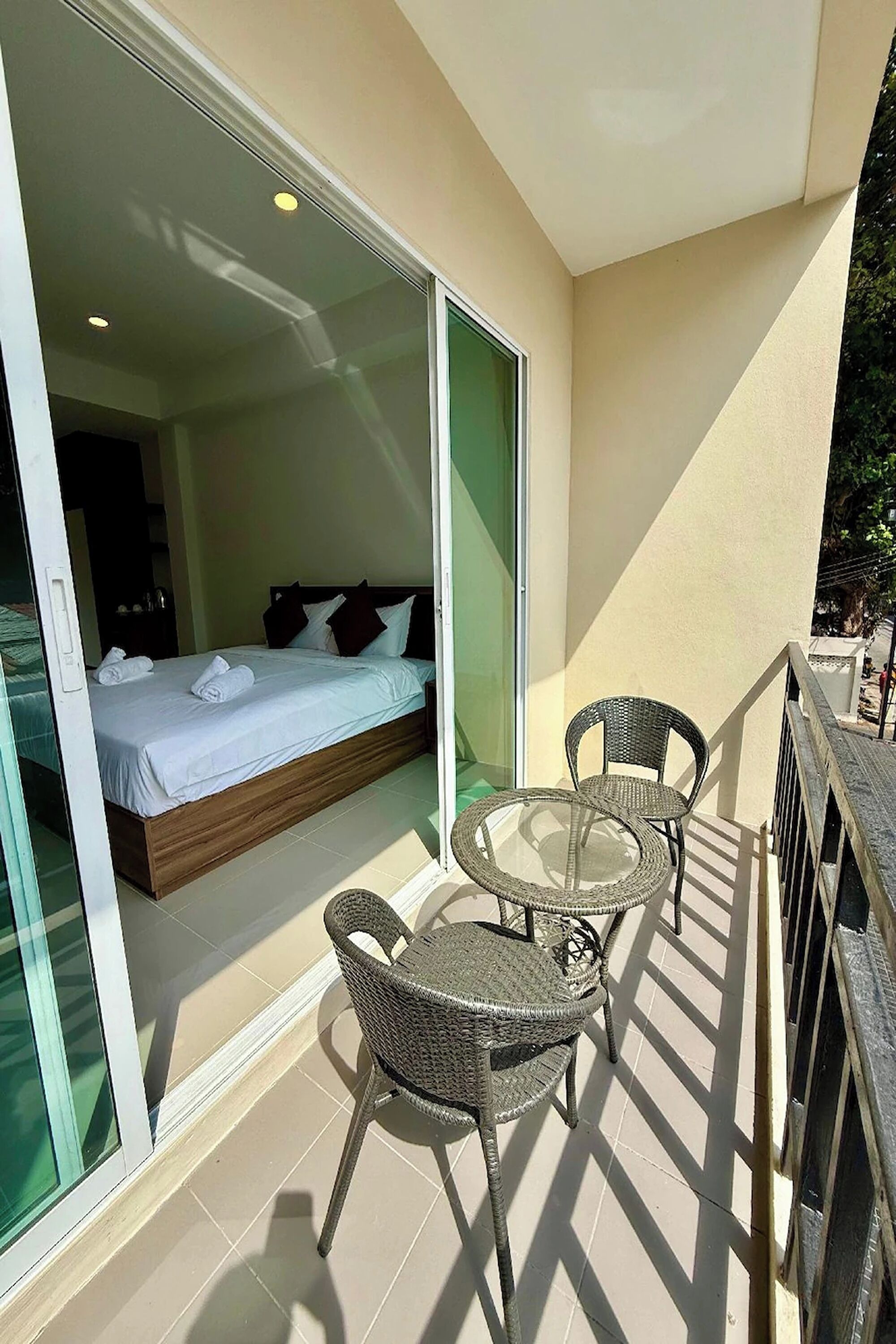 A balcony with a bed, two wicker chairs, and a glass door leading to a bedroom.
