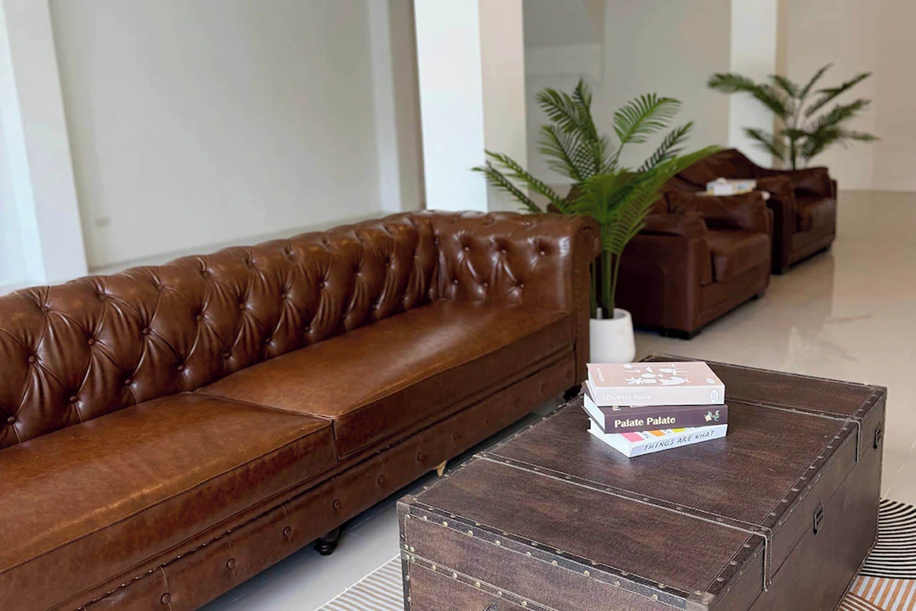 A brown leather sofa, a wooden coffee table with books, and two potted plants in a modern living room.