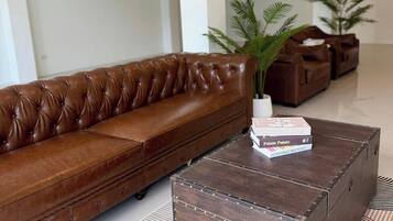 A brown leather sofa, a wooden coffee table with books, and two potted plants in a modern living room.