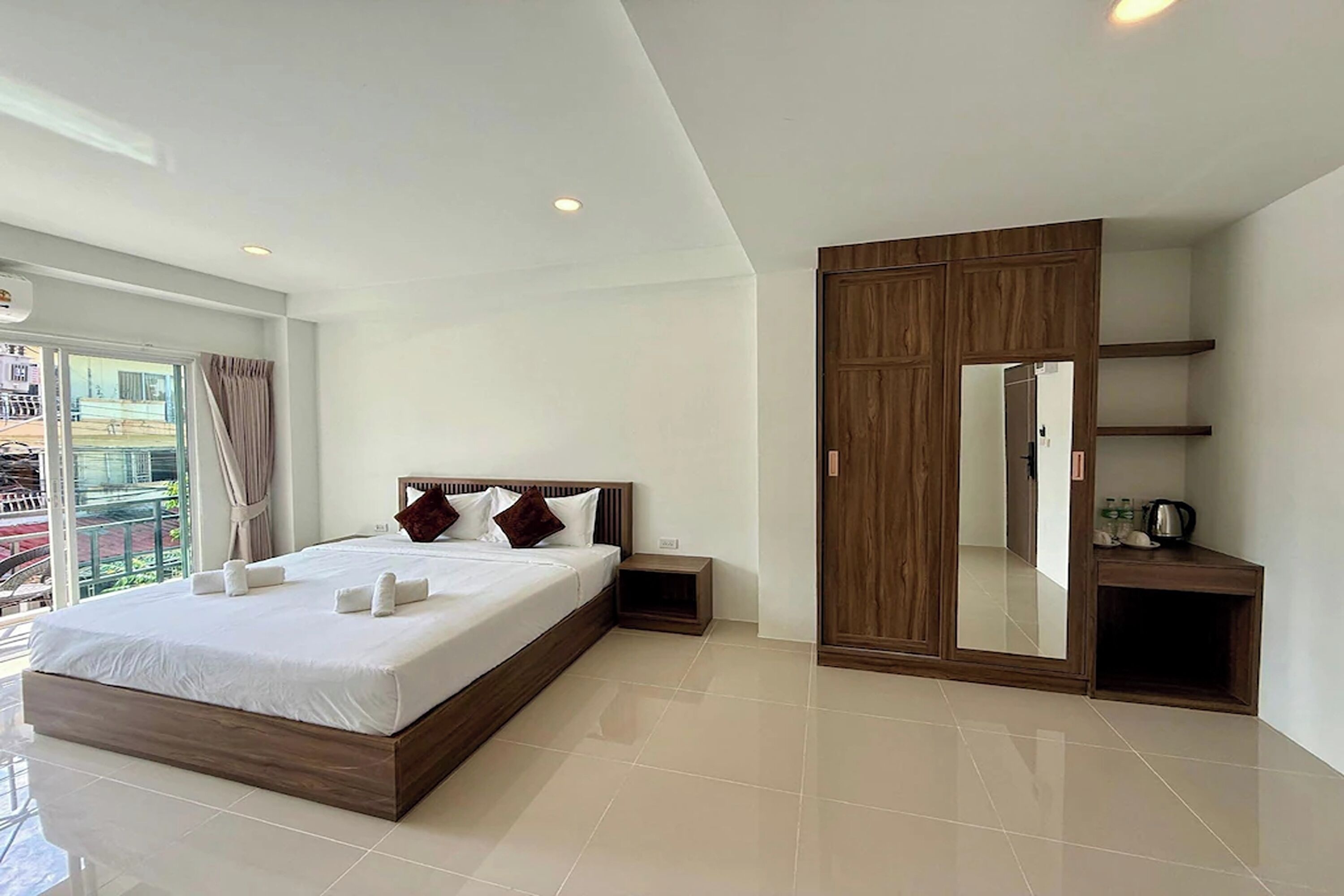 Une chambre d’hôtel moderne avec un grand lit, une armoire, une petite table de chevet et une grande fenêtre avec des rideaux.